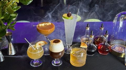 A spread of craft cocktails at The Flipside, smoke and garnishes under purple light